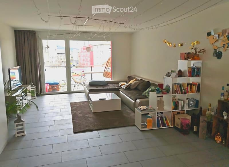 Modern living room with a grey sectional sofa, white coffee table, bookshelf, and large sliding glass doors leading to a balcony.