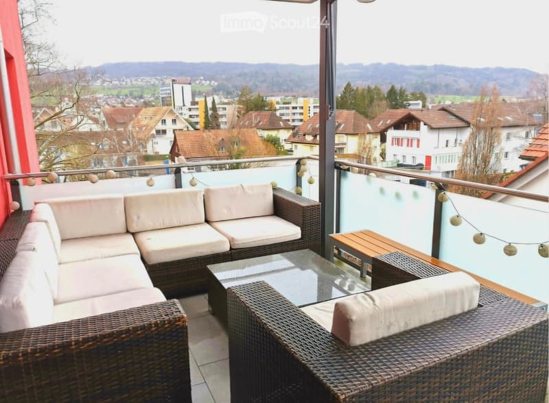 Balcony with wicker furniture, glass table, and scenic city view.