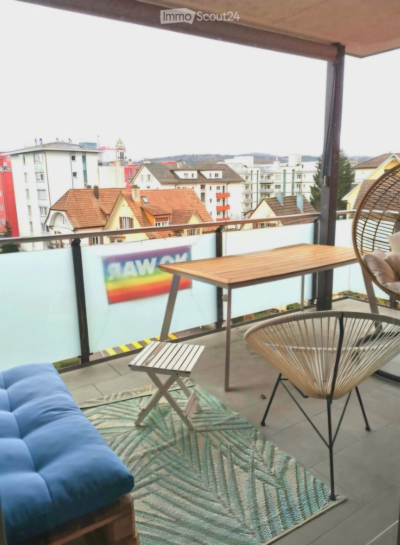 Balcony with a view of the city, featuring a wooden table, two chairs, and a blue sofa.