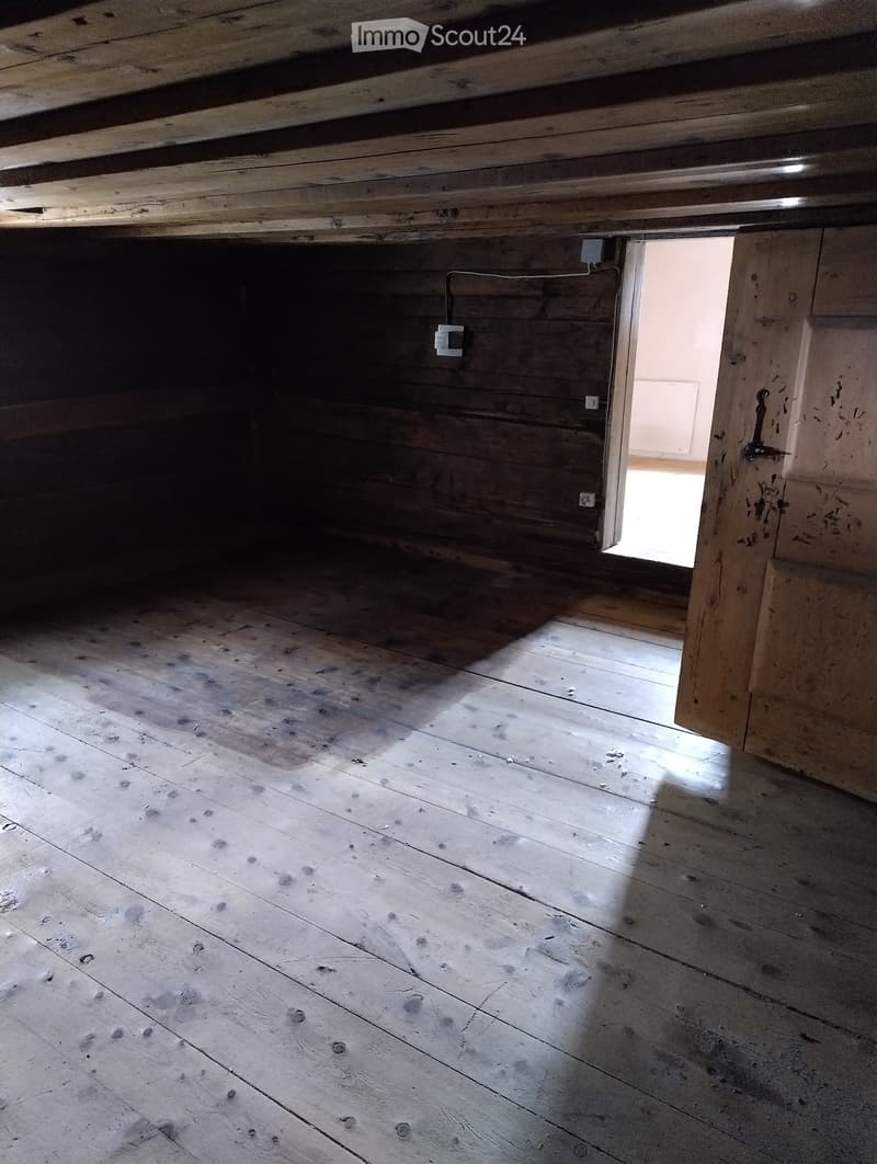 Empty room with wooden floor and exposed wooden beams on the ceiling. Natural light streams in from an open doorway.