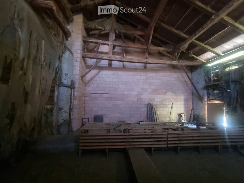 Empty room with exposed wooden beams and brick walls, featuring a large wooden workbench and scattered tools.