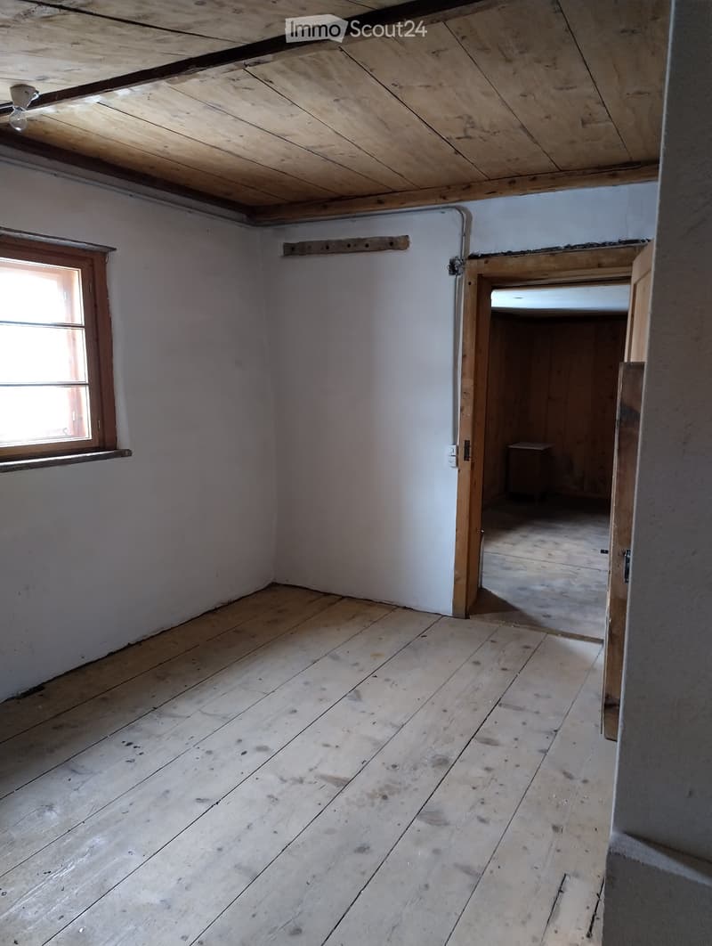 Empty room with wooden floor and white walls, featuring a single window and an open doorway leading to another room.