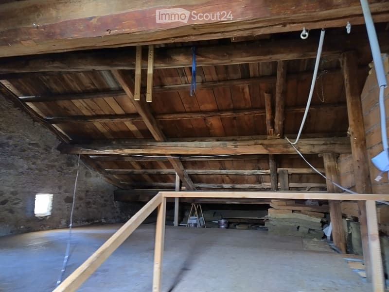 Empty attic space with exposed wooden beams and stone walls, concrete floor, and minimal construction materials visible.