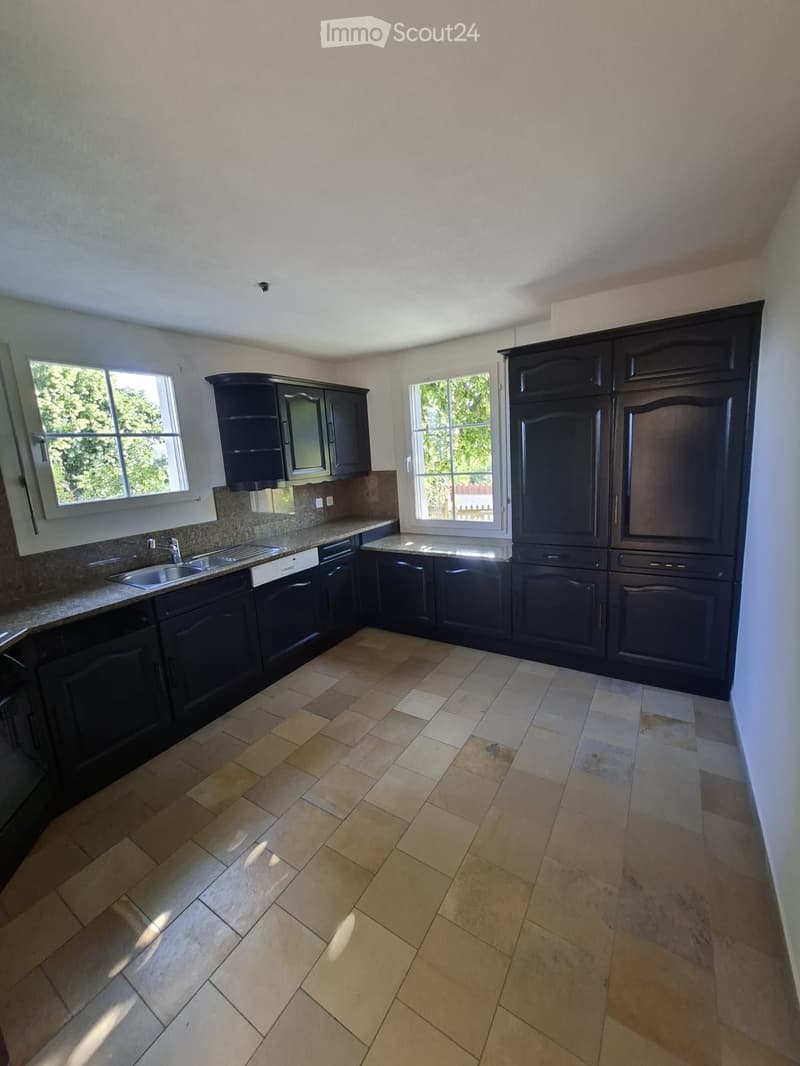 Empty kitchen with dark wooden cabinets, a tiled floor, and two windows letting in natural light.