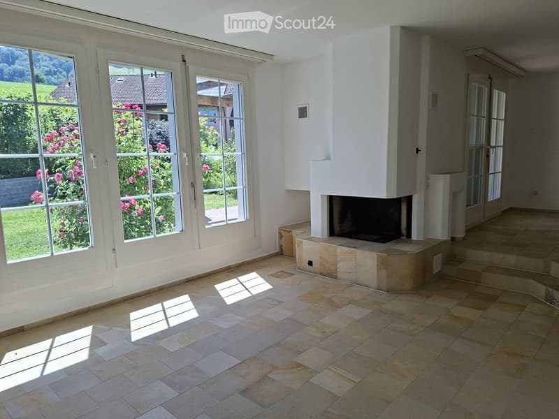 Bright, unfurnished room with large windows, tiled floor, and a built-in fireplace.