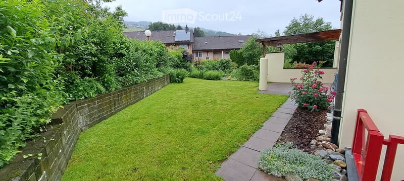 Well-maintained garden with a neatly trimmed lawn, a brick border, and a variety of plants and flowers. A covered patio area is visible in the background.