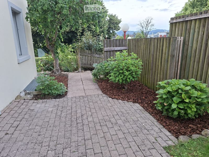 Garden area with a paved pathway, small plants, a wooden fence, and a streetlight.