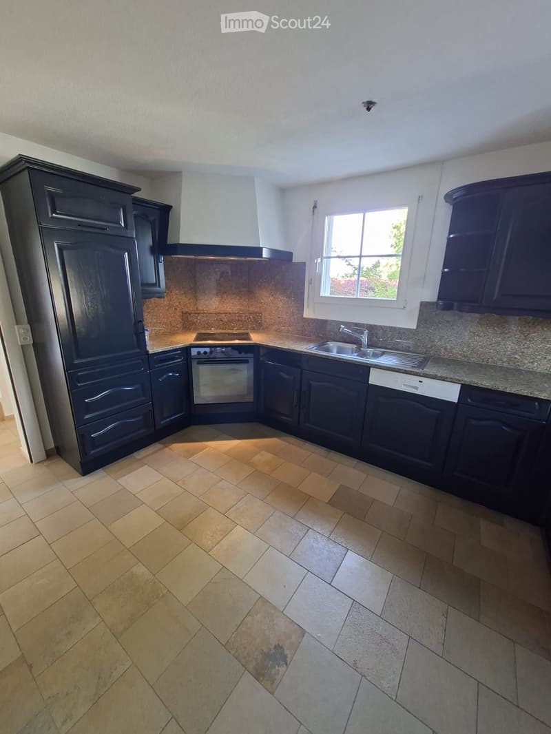Modern kitchen with dark cabinets, granite countertops, a stainless steel sink, and a refrigerator. The floor is tiled in a herringbone pattern.