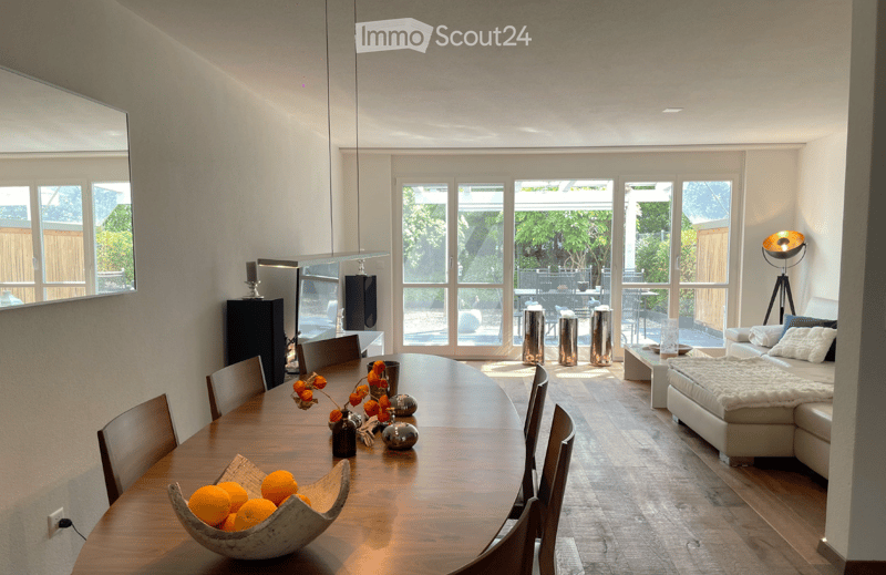 Open-plan living and dining area with large windows, modern furniture, and a view of the garden.