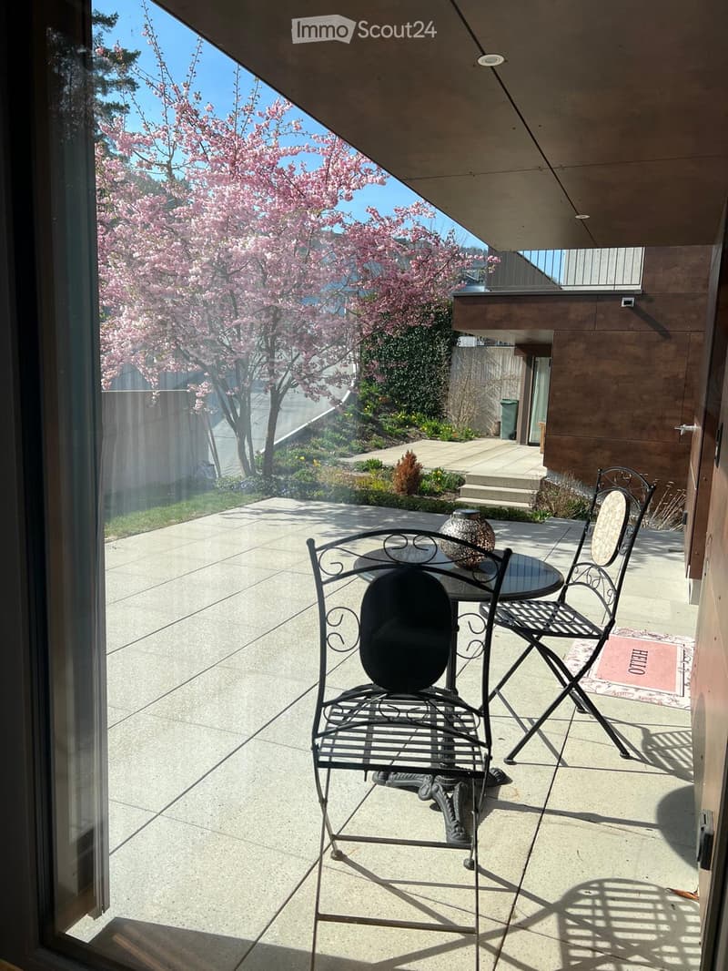 Balcony with a small table and two chairs, overlooking a garden with blooming trees and a pathway.