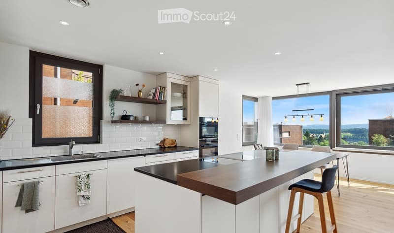 Modern kitchen with white cabinets, black countertops, large windows offering a scenic view, and a central island with bar stools.