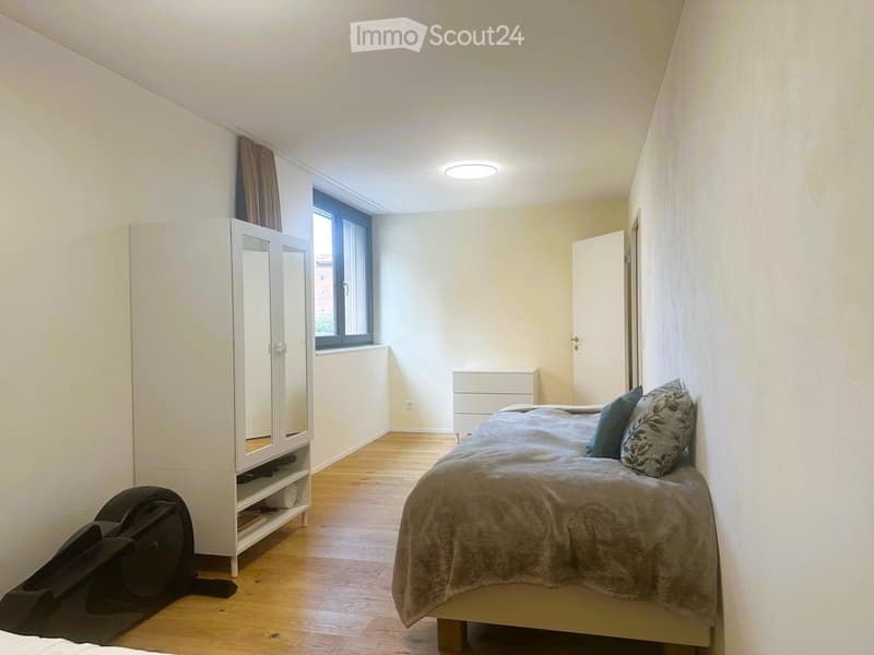 Bedroom with a single bed, wardrobe, nightstand, and a window with curtains. Wooden flooring and white walls.