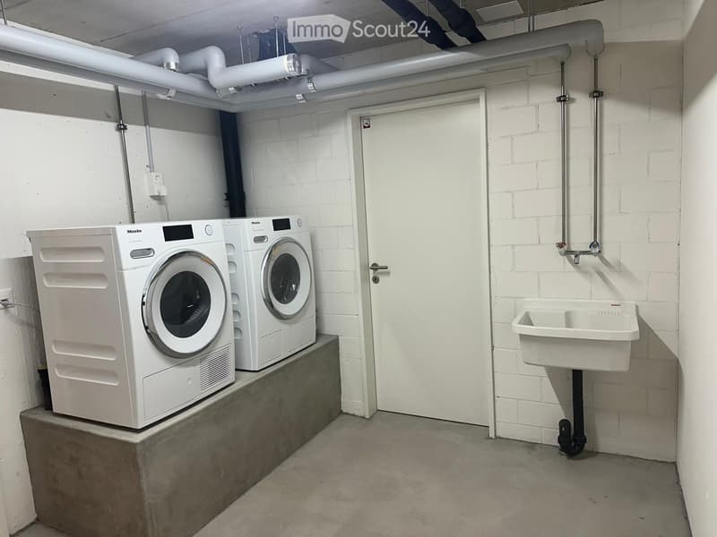 Utility room with a washing machine, dishwasher, and a sink, white brick walls, and a concrete floor.