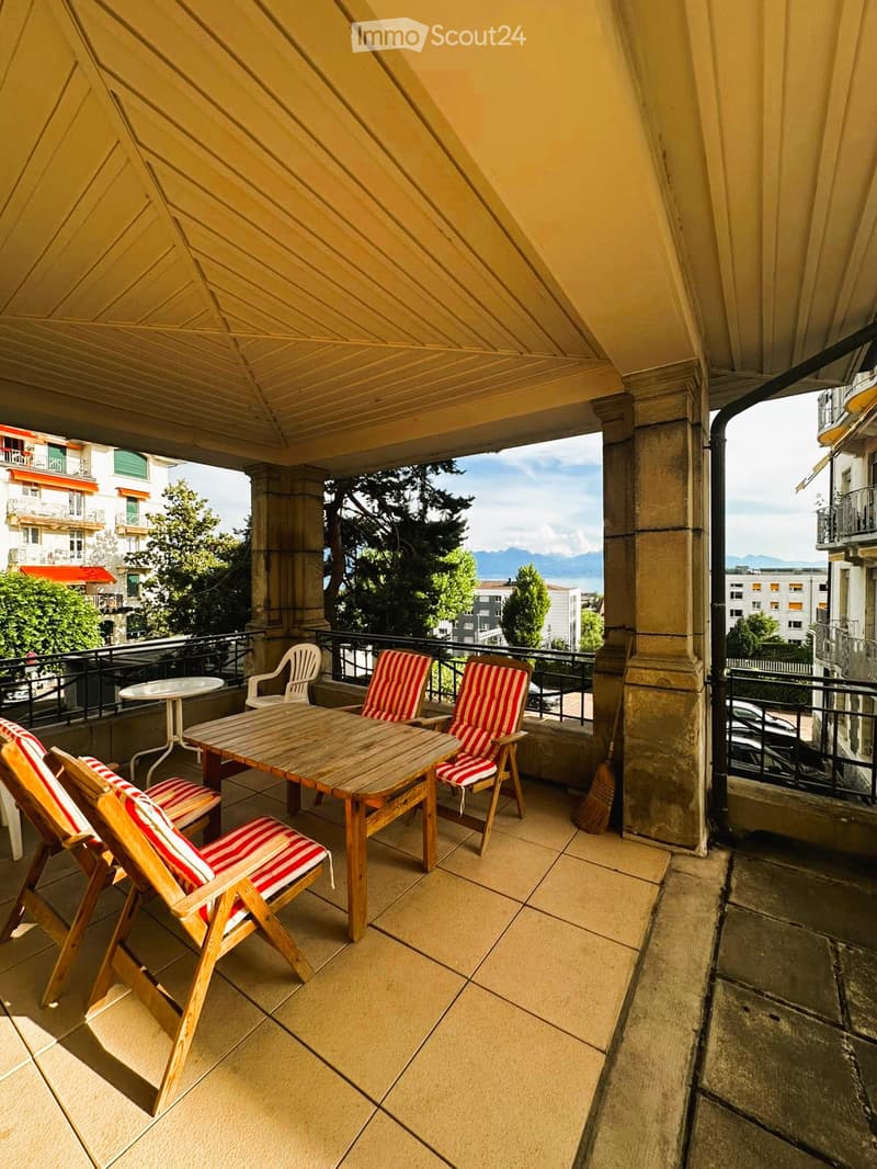 Balcony with wooden table and chairs, overlooking a scenic view of mountains and cityscape.