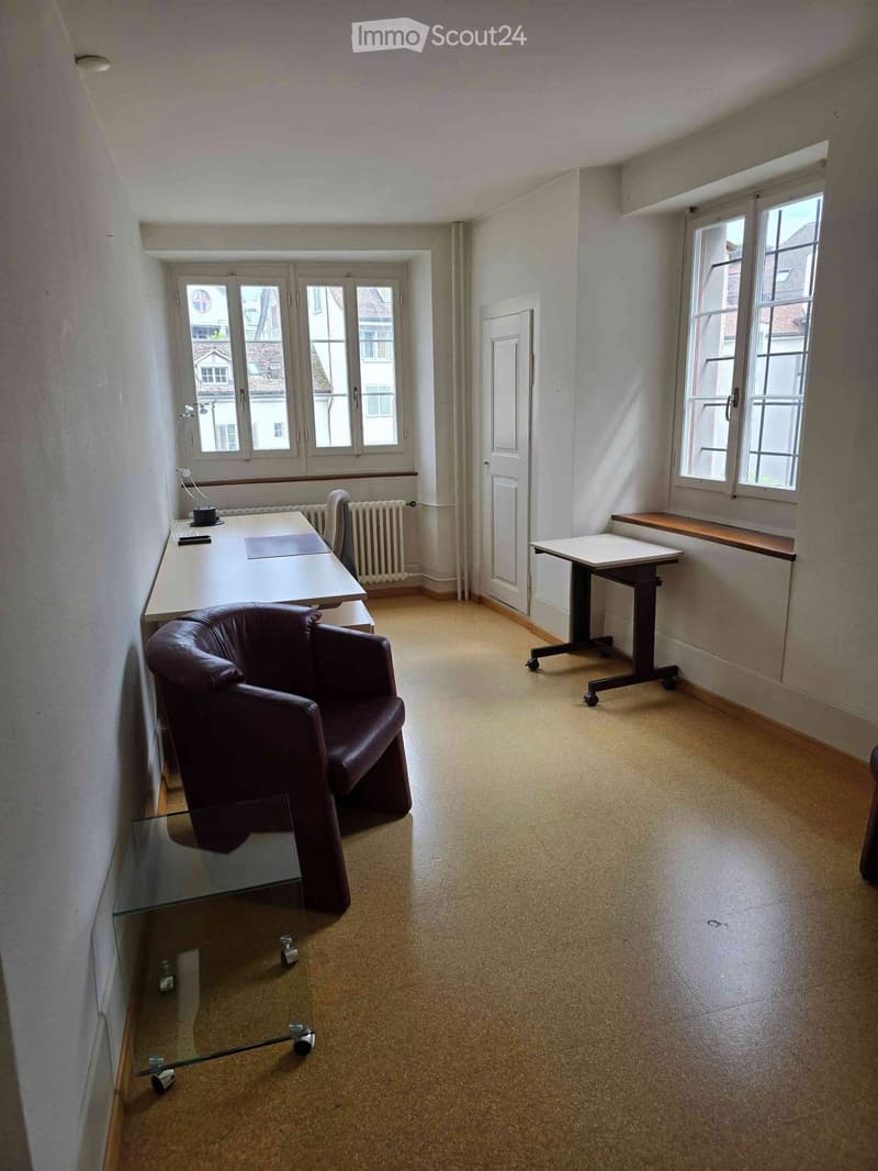 Office space with a brown leather chair, white desk, glass coffee table, and a small table near the window.