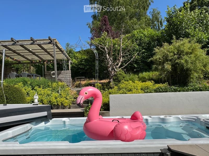 Garden area with a hot tub, pink inflatable flamingo float, covered patio, and lush greenery.
