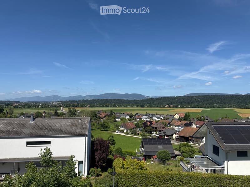 A rural village with scattered houses, green fields, and distant mountains under a clear blue sky.