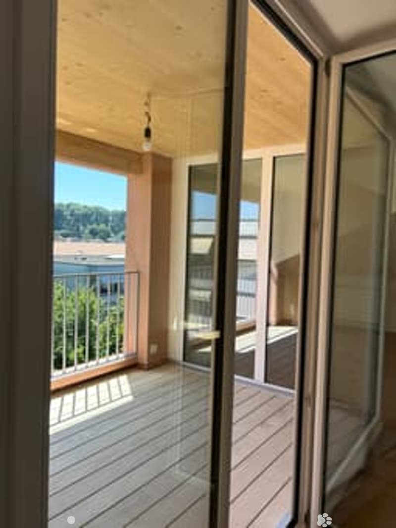 Spacious balcony with wooden decking, glass railings, and scenic city view.