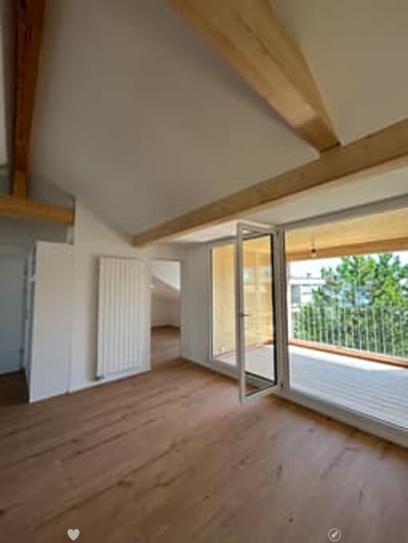 Bright, unfurnished room with wooden flooring, exposed wooden beams, large windows, and a balcony access door.