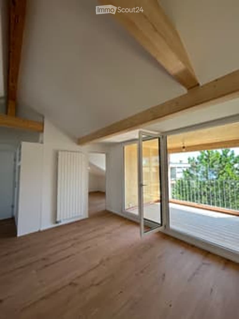 Bright, unfurnished room with wooden flooring, exposed wooden beams, large windows, and a balcony access door.