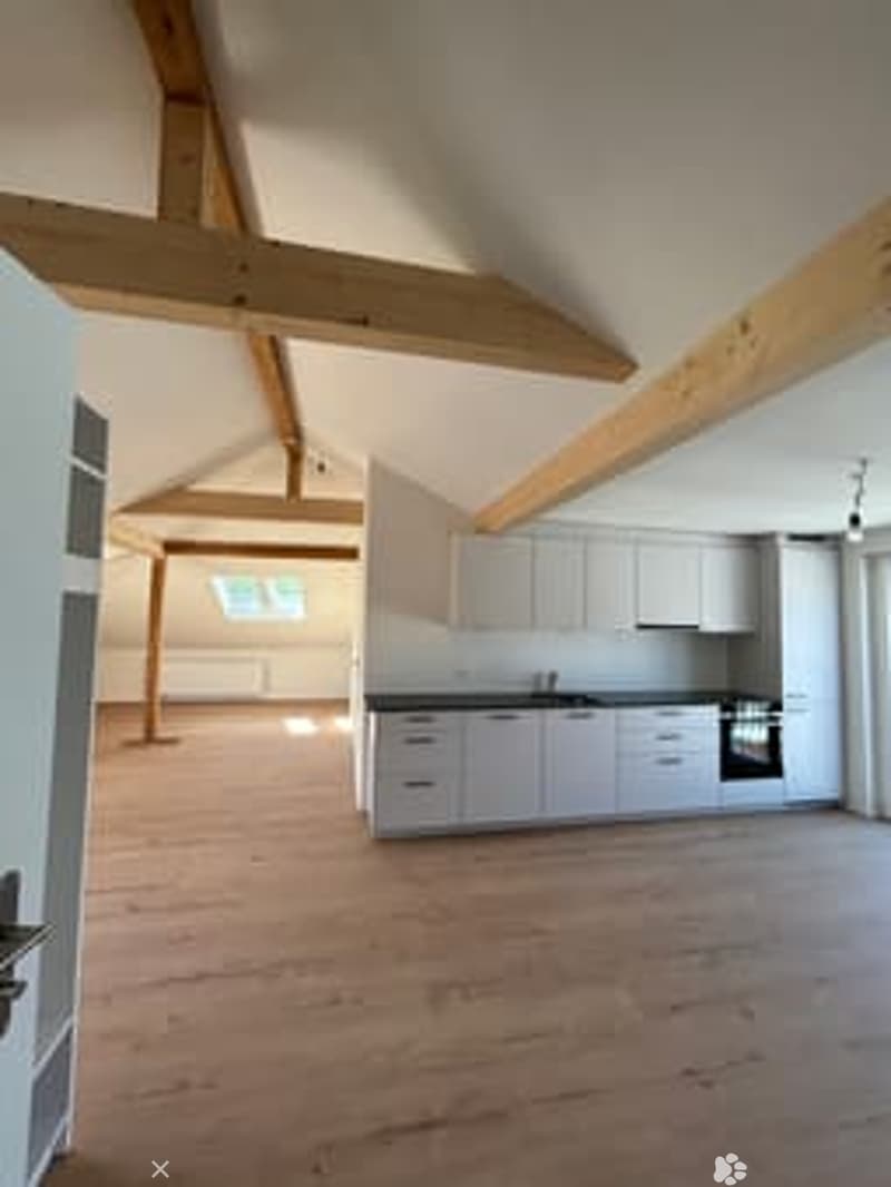 Bright, open kitchen with white cabinetry, stainless steel appliances, and exposed wooden beams on the ceiling. The floor is made of light wooden planks.