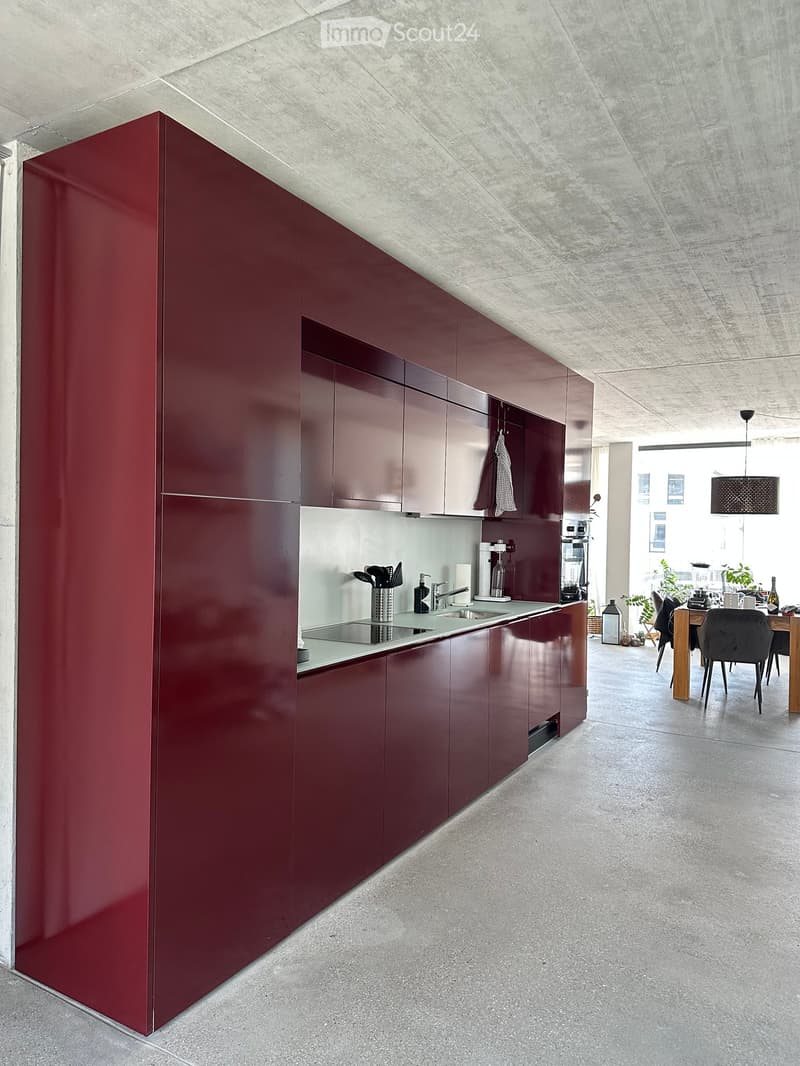 Modern kitchen with red cabinets, stainless steel sink, and a dining area with a table and chairs.