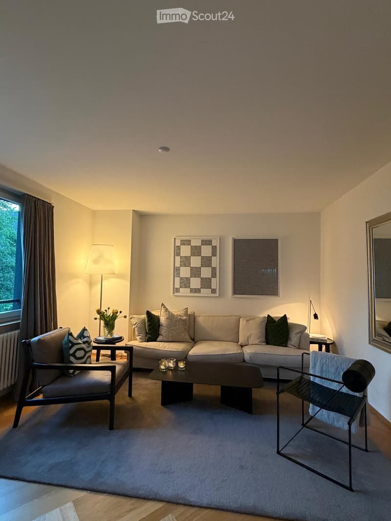 Modern living room with a large sectional sofa, coffee table, two armchairs, a floor lamp, and decorative artwork on the walls.