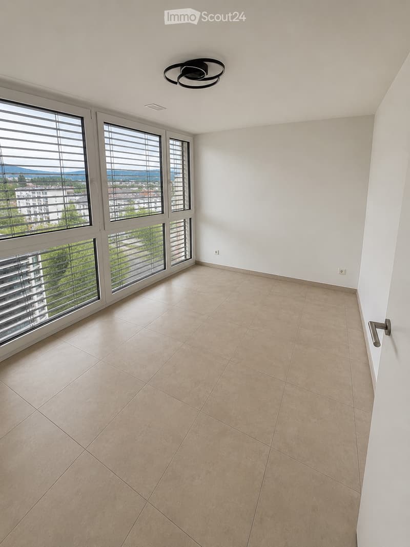 Empty room with beige tiled floor, white walls, large windows with blinds, and a modern ceiling light fixture.