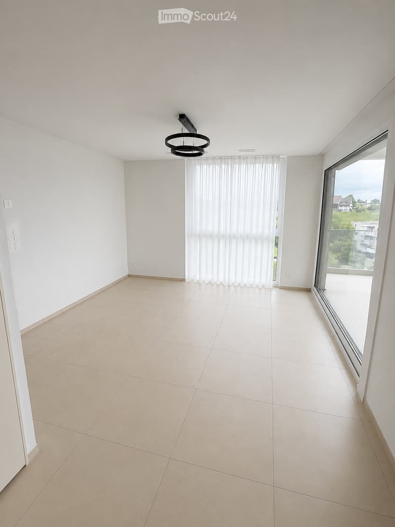Empty room with tiled floor, white walls, large window with blinds, and a modern ceiling light fixture.