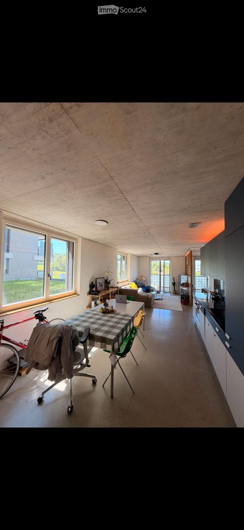 Open-plan living and dining area with modern kitchen, large windows, and wooden ceiling.