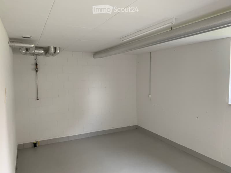 Empty room with white walls, grey floor, exposed pipes, and a single window