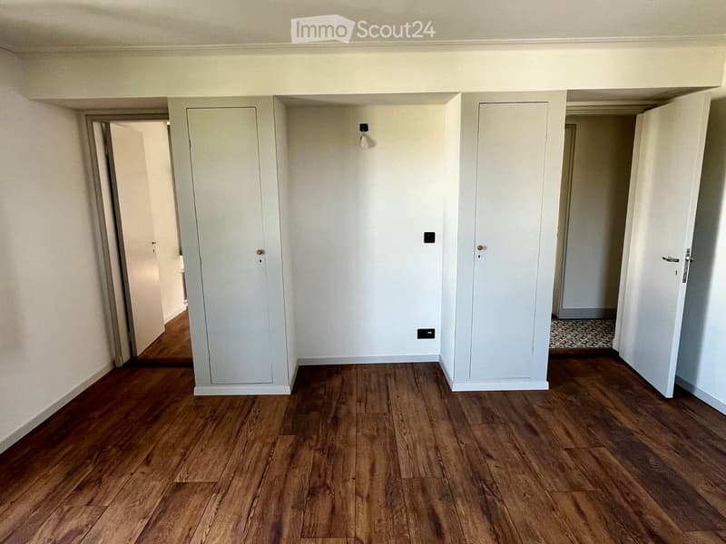 Empty room with wooden flooring, white walls, and several doors leading to other spaces.