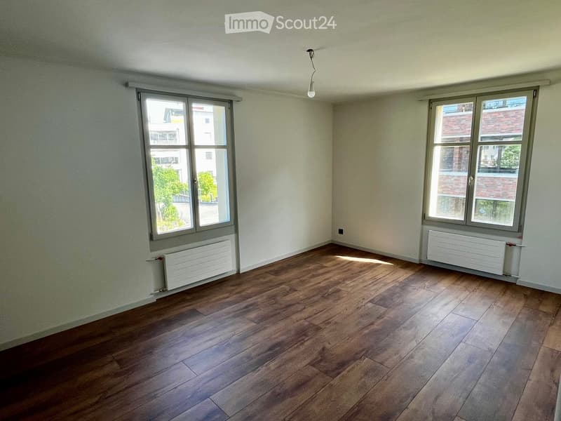 Empty room with wooden flooring, white walls, and two windows with radiators below them.