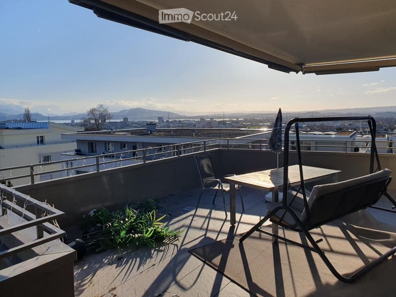 Balcony with a view of the city and mountains, featuring a table, chairs, and an umbrella.