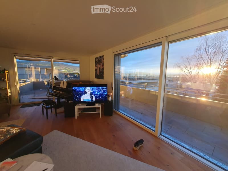 Modern living room with large windows offering a scenic view, featuring a sofa, coffee table, piano, television, and floor lamp.
