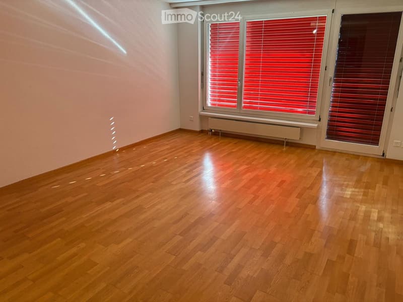 Empty room with wooden flooring, white walls, and large windows with red blinds. No furniture or equipment present.