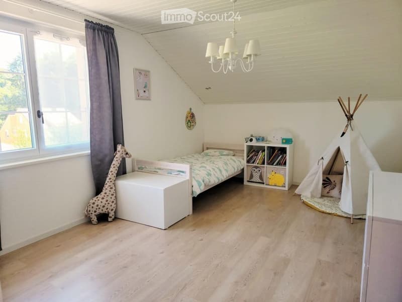 Bright, cozy children's bedroom with wooden flooring, a single bed, a teepee tent, a bookshelf, and a stuffed giraffe toy. The room features large windows with curtains and a chandelier.