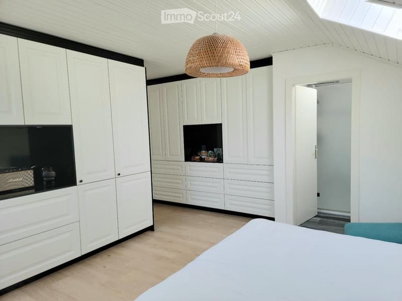 Modern kitchen with white cabinets, a pendant light, and a small table. The space features a sleek design with a neutral color palette and a clean, organized layout.