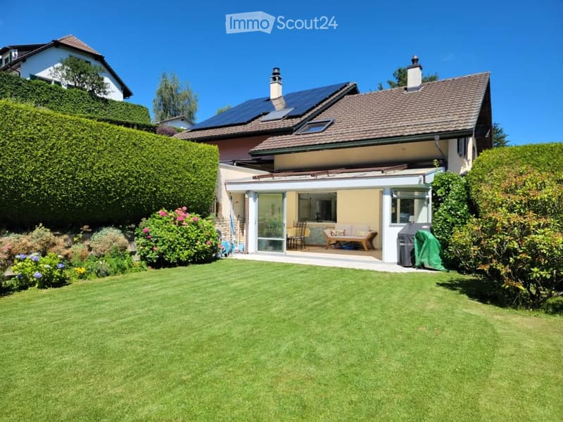 Two-story house with a well-maintained garden, solar panels on the roof, and a covered patio area with outdoor furniture.