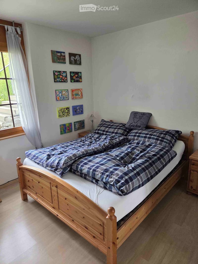 Cozy bedroom with a wooden bed, plaid bedding, nightstand, and decorative wall art.