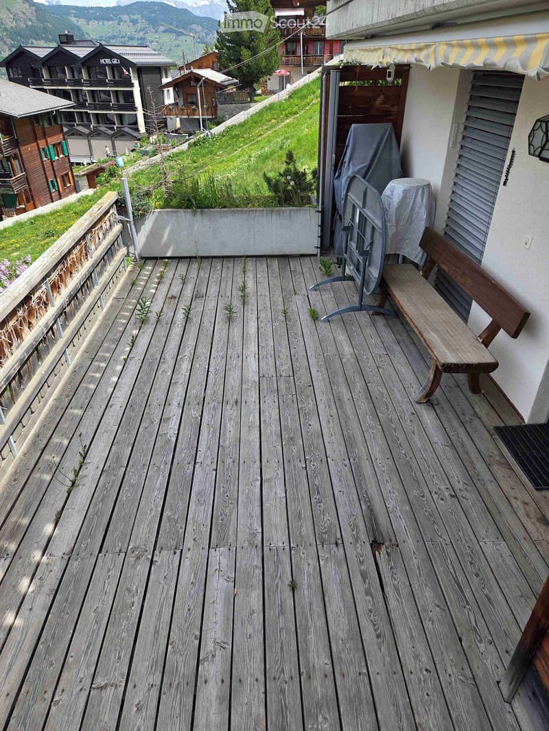 Wooden balcony with a bench, overlooking a grassy area and distant mountains.