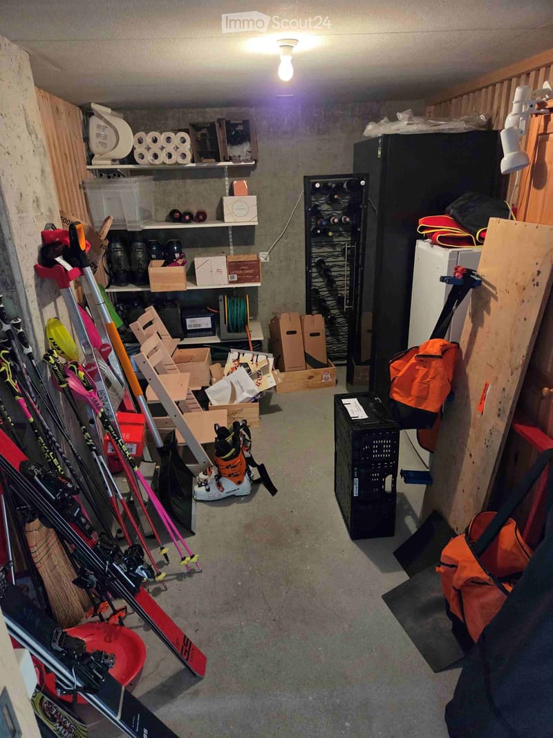 A well-organized storage room with skis, snowboards, a wine rack, a refrigerator, shelves, boxes, and various storage items.