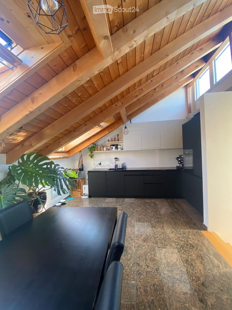 Open-plan kitchen and dining area with dark cabinets, granite flooring, and a high wooden slanted ceiling with skylights.