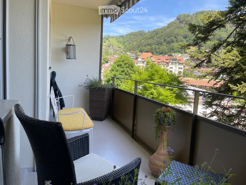 Balcony with wicker chairs, small table, potted plants, and scenic mountain view.