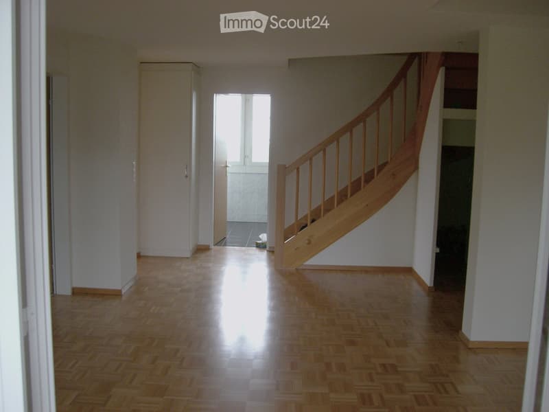 Empty hallway with wooden flooring, white walls, and a staircase leading upwards.