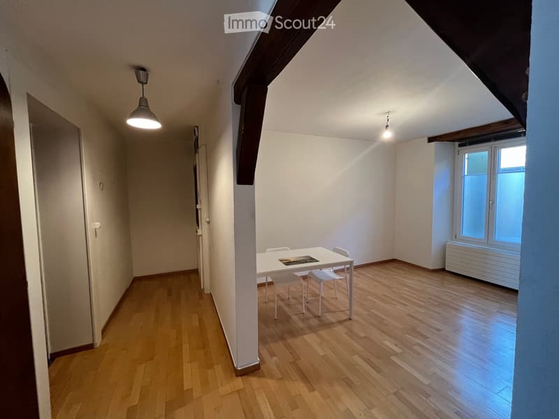 Bright, unfurnished room with wooden flooring, white walls, and a small table with chairs near a window.