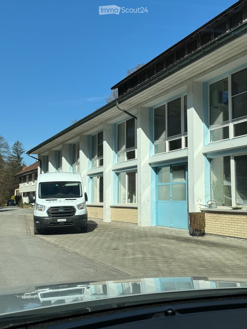 Two-story building with light blue and white exterior, large windows, and a garage entrance. A white van is parked in front.