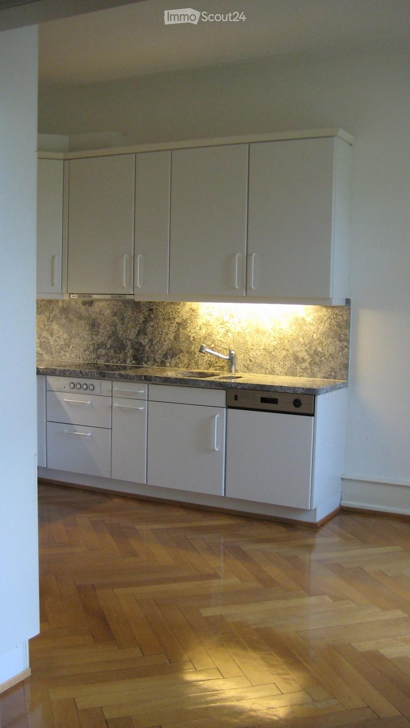 Modern kitchen with white cabinets, granite countertop, and wooden flooring.