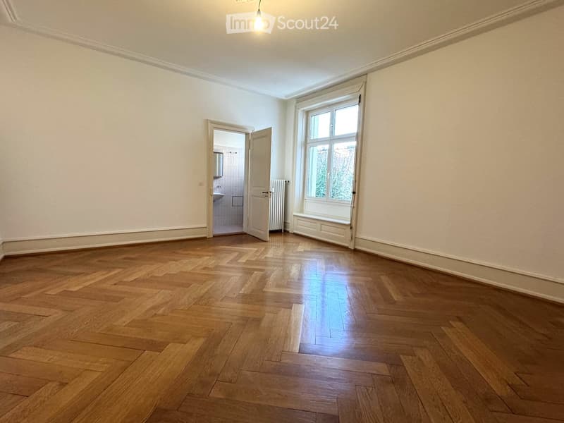 Empty room with wooden flooring, white walls, large window, and an open door leading to a bathroom.
