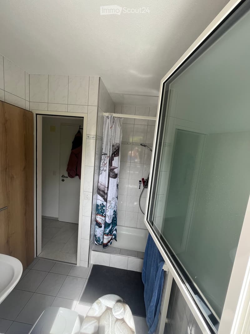 Modern bathroom with a white tiled wall, a bathtub with a shower curtain, a sink, a mirror, and a towel hanging on the side.